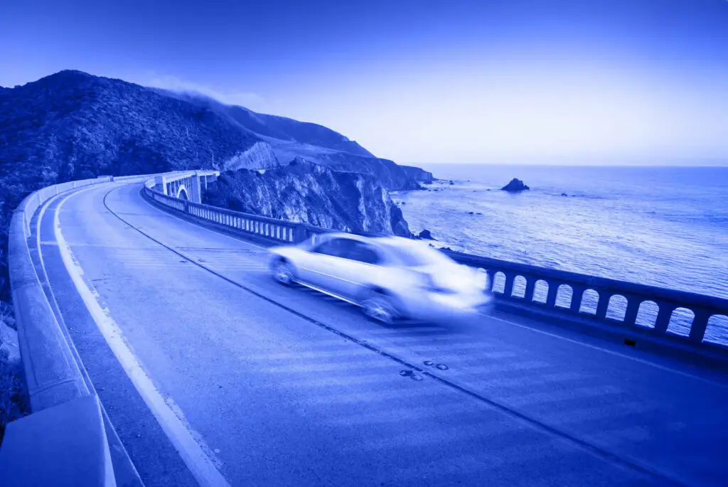 Car driving along a coastal mountain road with ocean view