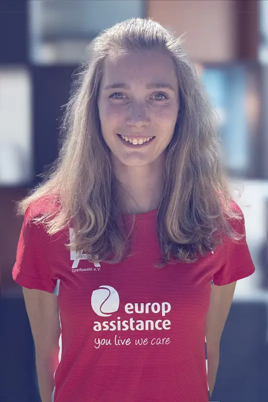 Person wearing a red Europ Assistance T-shirt with the slogan 'You live we care', standing indoors.