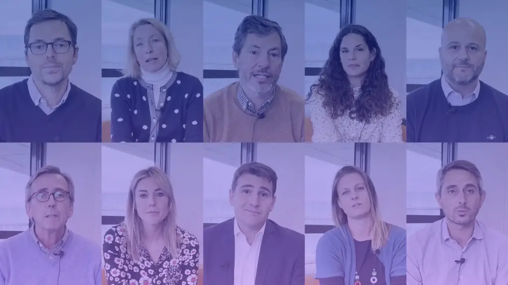 Group of ten people seated indoors in two rows, wearing business casual clothing, with large windows in the background